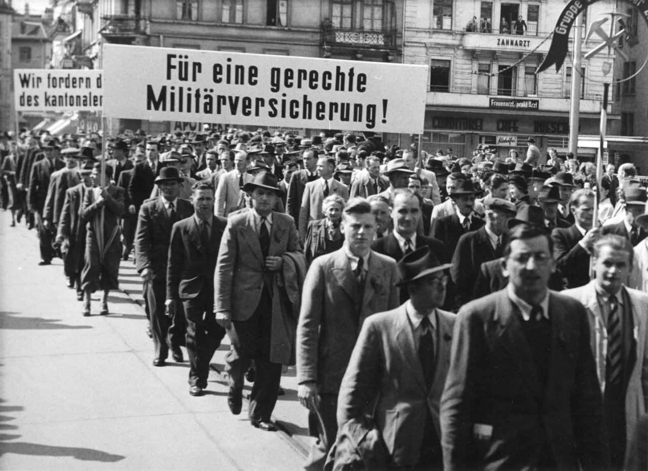 Corteo del primo maggio con uno striscione: “Per un’assicurazione militare giusta!”. Fonte: Archivio sociale svizzero, Zurigo, Sozarch_F_5047-Fb-090.